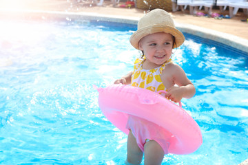 Happy little girl playing with colorful inflatable ring in the outdoor pool . Children learn to swim. Children's water games.Family beach vacation.