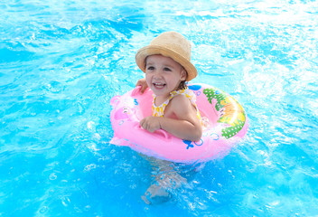 Fototapeta na wymiar Happy little girl playing with colorful inflatable ring in the outdoor pool . Children learn to swim. Children's water games.Family beach vacation.