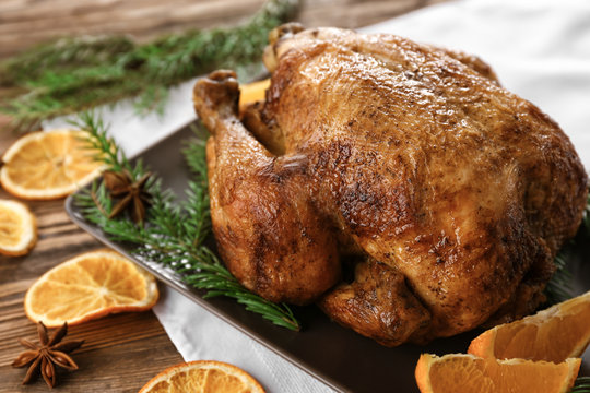 Tasty whole roasted turkey with sliced orange and coniferous branches on table