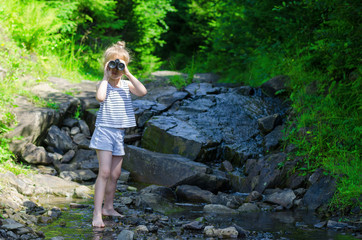 A little girl looks through binoculars, a beautiful landscape, free space.