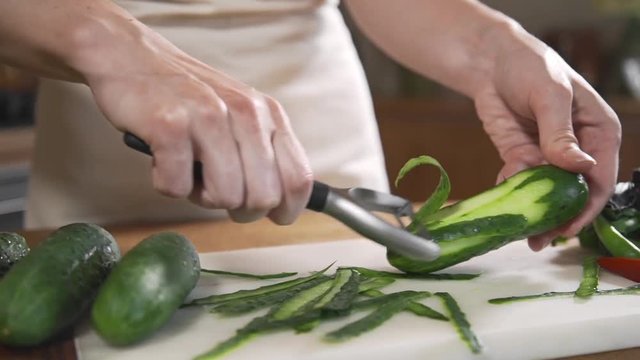 Chef peels cucumbers fof making vegetable salad with fresh greens, vegetarian dishes, cooking food, healthy nutrition
