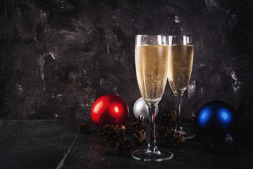 Dry Champagne in glasses, Christmas colorful balls, pine cones, New Year still life composition on dark stone background, selective focus copy space