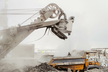 Excavator loading into a big mining dump truck. Work in heavy industry.
