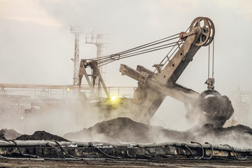 Big bucket excavator works in a outdoors dust dump. Industrial background.