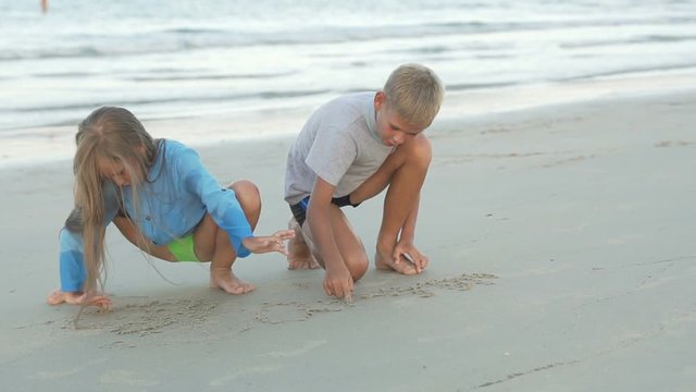 Little boy and girl draw on sand.