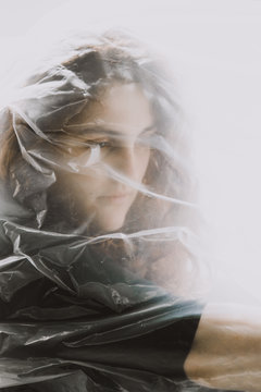 A portrait of a redhead woman resting behind a sheet of plastic