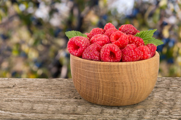 Raspberry in a wooden bowl on table with a blurry garden background