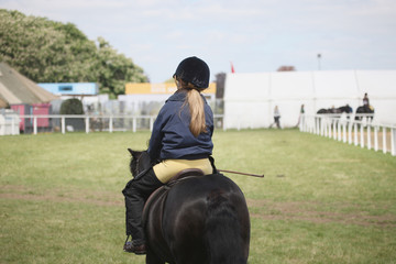 A girl in a jockey uniform riding a pony