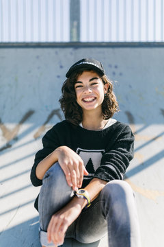 Smiley teen-age girl black sweater sits in a skate park.
