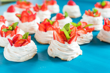 A small meringue Pavlova dessert with some strawberry slices with mint leaves on a blue background
