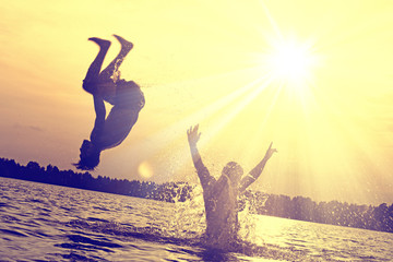 Glückliche junge Menschen laufen und springen am See beim Sonnenuntergang