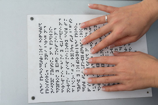 Hands of a girl reading a text written on Braille. People