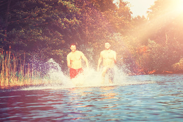 Glückliche junge Menschen laufen und springen am See beim Sonnenuntergang