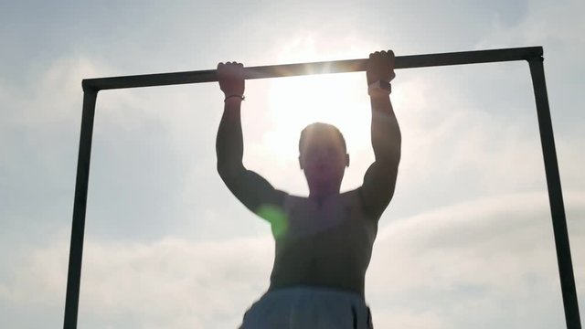 Athlete man doing pull ups on a bar against a background sun rays