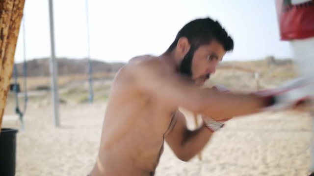 Bearded man fighter making blows on combat bag. Boxing training