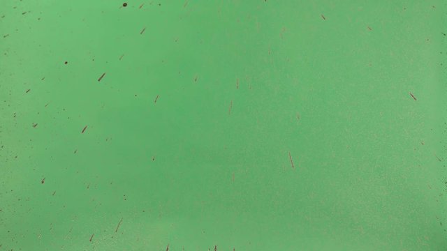 Red ink sprinkled over green screen background. Close-up shot