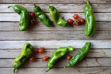 Some cherry tomatoes and green peppers on a wooden table of a rustic kitchen. Top view. Empty copy space for editor's text.