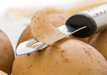Potatoes, with a vegetable peeler on a white background, close up