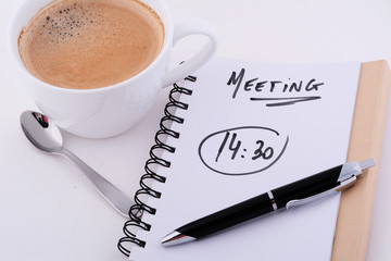 Notepad with text "MEETING 14:30" with cup of coffee.