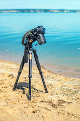 Camera on a tripod near the seaside removes of seashells on the sand. Photographic equipment in the process of shooting the landscape. Camera while taking a photo or time-lapse