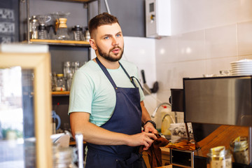 Fototapeta premium Portrait of a young male baristas at a bar counter near a coffee machine