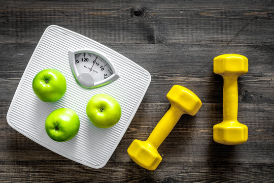 Sport and diet for losing weight. Bathroom scale, apple and dumbbell on wooden background top view
