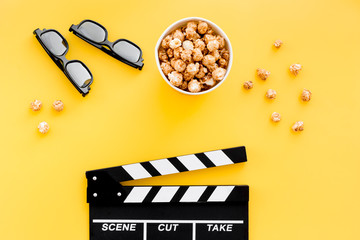 Ready to watch film. Clapperboard, glasses and popcorn on yellow background top view