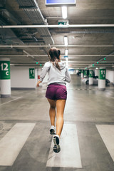 Beautiful athletic woman running in a public parking garage. 