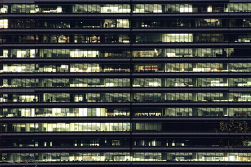 Mehrstöckiges Bürogebäude in der Nacht mit Arbeitern, die Überstunden machen. bis spät in die Nacht im Büro. Beleuchtung und arbeitende Menschen im Inneren. Späte Überstunden in einem modernen Bürogebäude