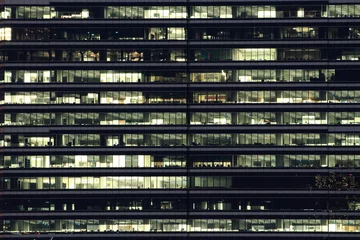 Fototapete Stadtgebäude Mehrstöckiges Bürogebäude in der Nacht mit Arbeitern, die Überstunden machen. bis spät in die Nacht im Büro. Beleuchtung und arbeitende Menschen im Inneren. Späte Überstunden in einem modernen Bürogebäude