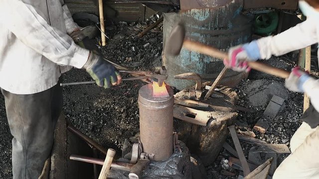 Two blacksmiths forging an axe's head by hitting red-hot steel with a hammer