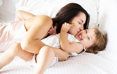 Mom and daughter are playing in the morning in bed