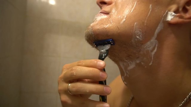Adult man shaving with foam and manual razer.