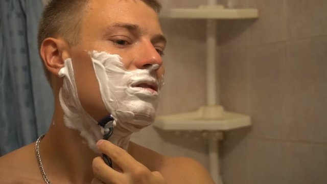 Adult man shaving with foam and manual razer.