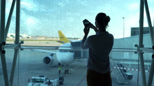 Silhouette of woman taking photos with cellphone in lobby at airport 
