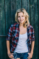 Fototapeta premium Beautiful young woman looking at camera, wooden barn wall on the background. Female portrait.