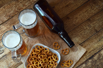 Football fan set with mugs of beer, bottle and salty snacks on wooden background. Junk food for beer or cola. Photographed with natural light.