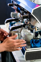Asian barista steaming fresh milk in stainless pitcher with vent pipe