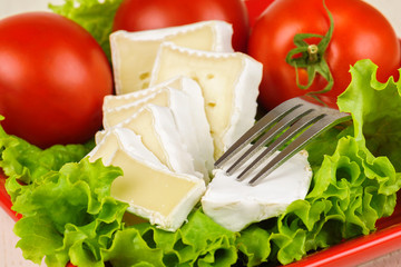Tomatoes and cheese slices lie on a sheet of fresh salad in a red plate.