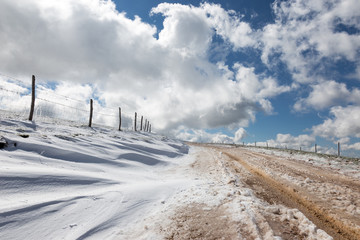 A mountain road with snow at the side, under a deep, blue sky with white clouds
