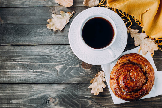 Fresh Pastry Bun, Cup of hot coffee and autumn leaves on wooden background. Top view, copy space