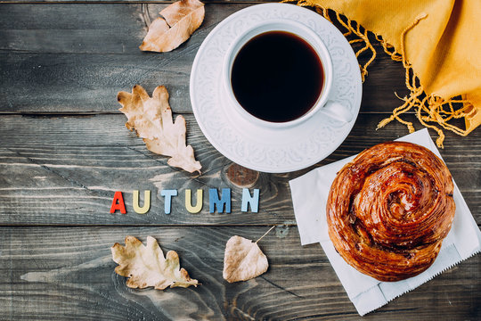 Fototapeta Fresh Pastry Bun, Cup of hot coffee and autumn leaves on wooden background. Wooden letters wod AUTUMN. Top view, copy space