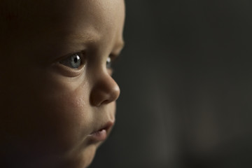 Portrait of serious one year toddler on the dark background. Close-up view. Copy space