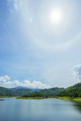 Lake with Mountains.Relax summer wallpaper, daytime landscape with lake among the wooded green mountains, beautiful blue cloudy sky and fantastic beautiful sun halo phenomenon in Thailand.