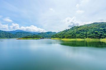 Fototapeta na wymiar Lake with Mountains.Relax summer wallpaper, daytime landscape with lake among the wooded green mountains, beautiful blue cloudy sky. Khun Dan Prakan Chon Dam,