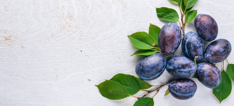 Plums with green leaves. On a wooden background. Top view. Free space for text.