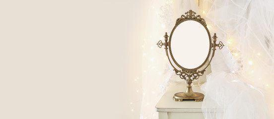 Old vintage oval mirror and beautiful white wedding dress and veil on chair with gold garland lights