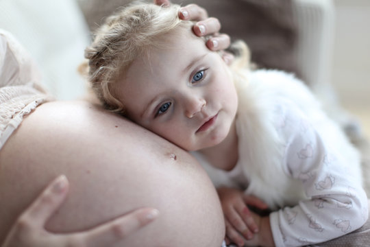 cute big sister listening to mother's unborn baby kicking, family moment