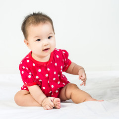 Portrait of adorable baby sitting on a white floor and smiling with copyspace