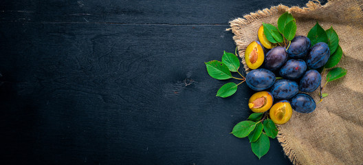 Plums with green leaves. On a wooden background. Top view. Free space for text.